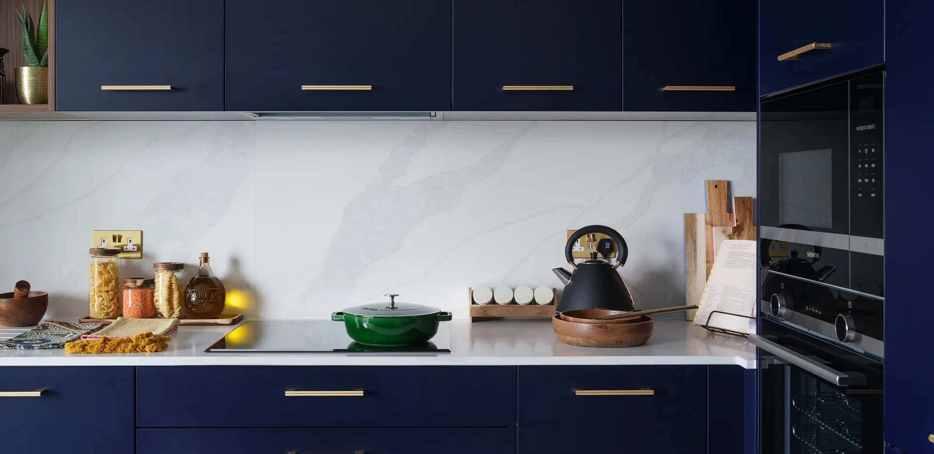 Modern navy blue kitchen featuring marble splashback, brass handles, and sleek built-in appliances.
