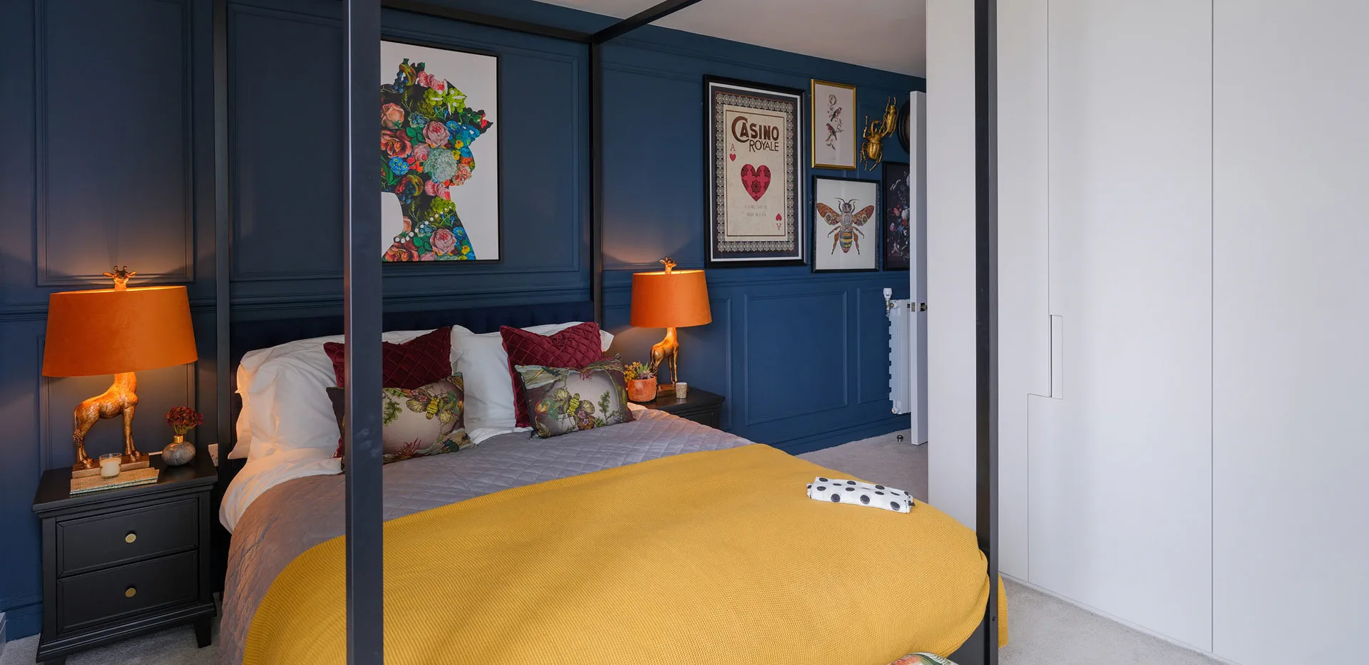 Chic bedroom with a four-poster bed, dark blue panelled walls, yellow throw, and unique lighting.