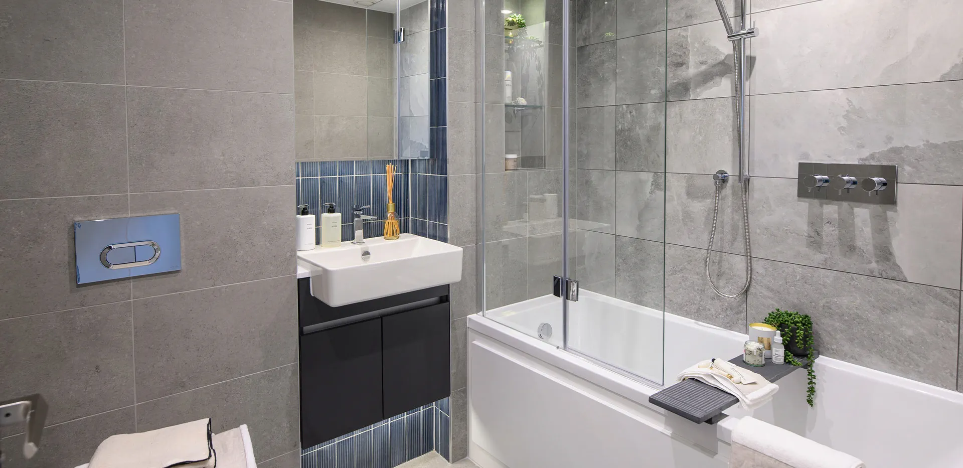 Contemporary bathroom with sleek grey tiles, blue accent wall, bathtub shower, and floating vanity.