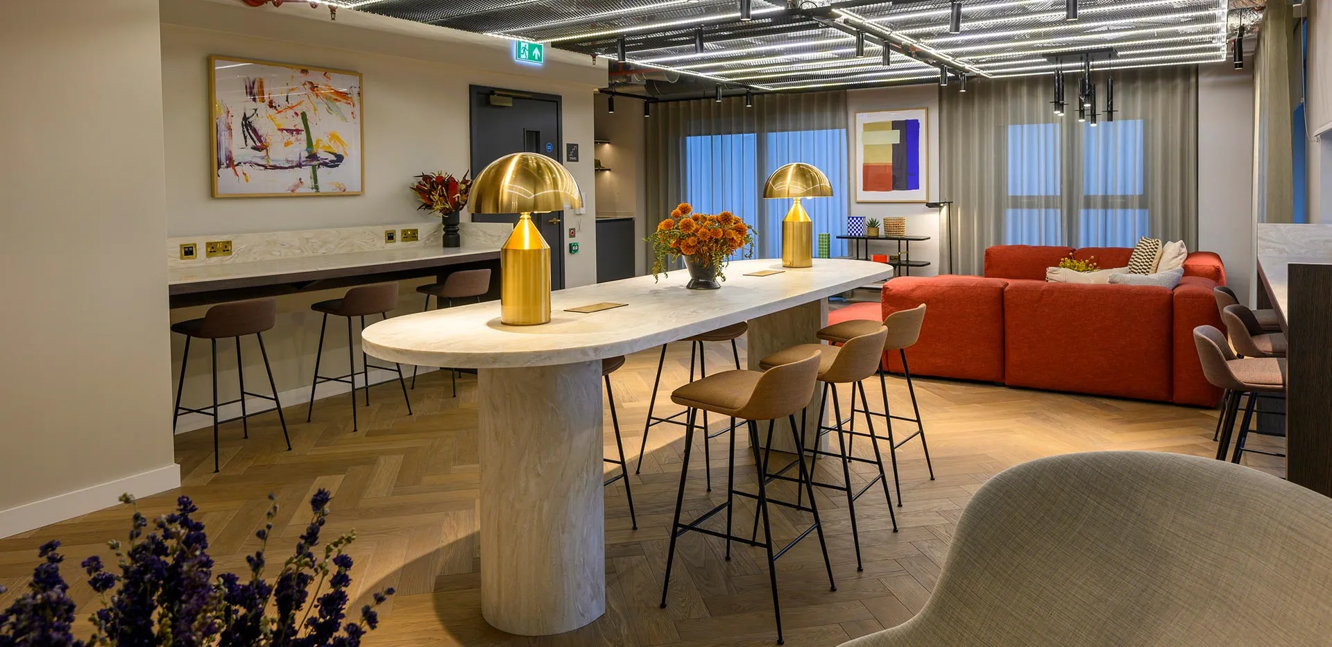 Spacious resident's lounge with co-working table, red sofa, and modern art at The Exchange Watford