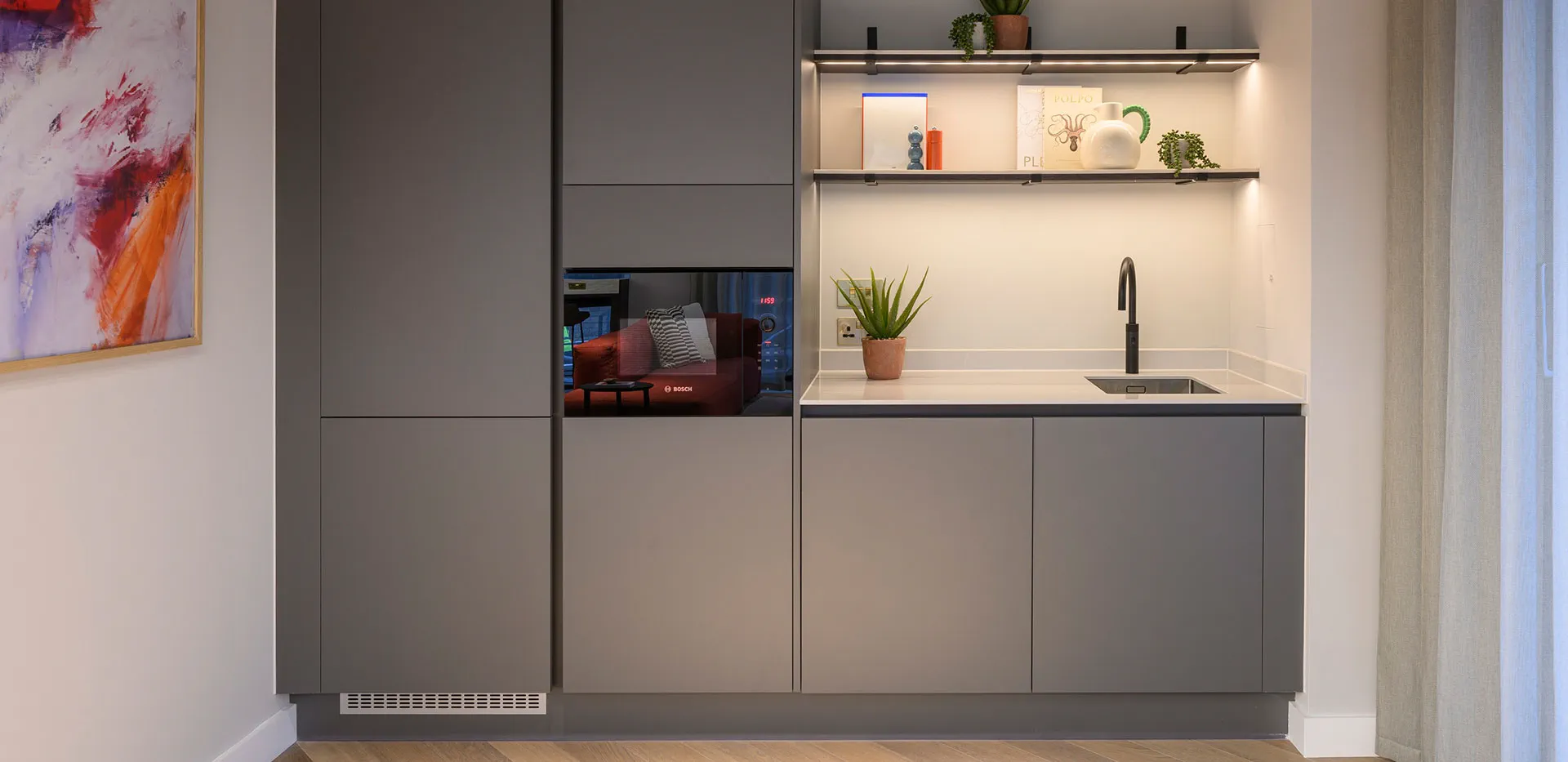 Modern dark gray residential kitchen with integrated appliances, shelves, and a view of the lounge