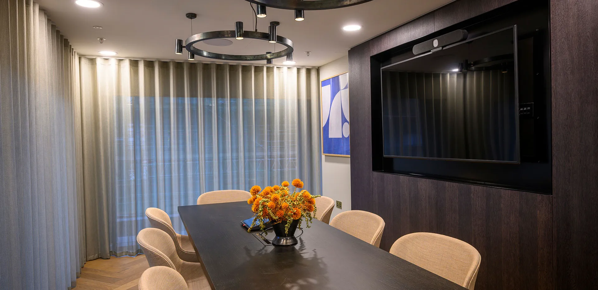 Elegant residential dining or meeting room with black table, orange flowers, and integrated TV